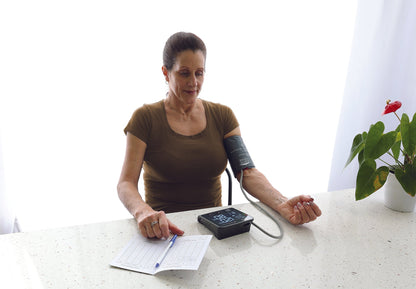 Patient sitting at a table and taking her blood pressure with the BD252 monitor