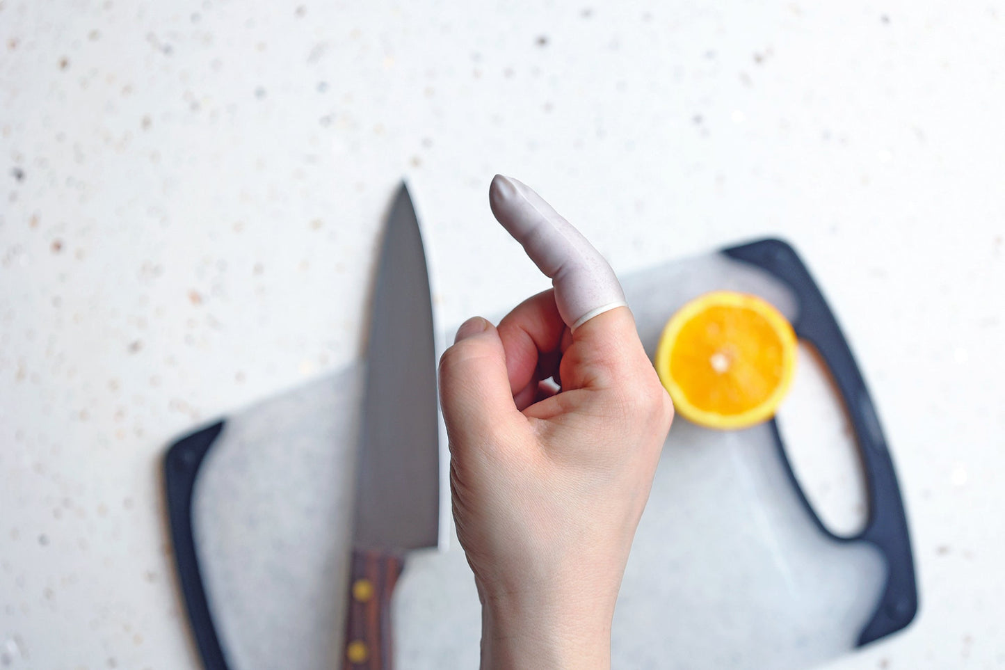 a hand with one finger wearing a finger cot with a knife and a cutting board on the background